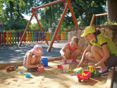 Kinderen spelen met zand speelgoed in een zandbak op een speelplaats naast een schommel.