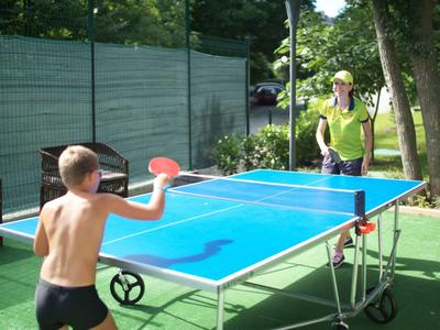 Twee personen spelen buiten tafeltennis op een blauw tafeltennistafel bij mooi weer.
