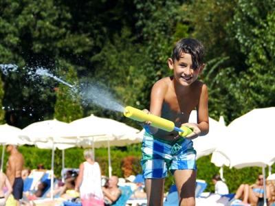Jongen speelt met tuinslang bij zwembad naast ligstoelen en parasols.