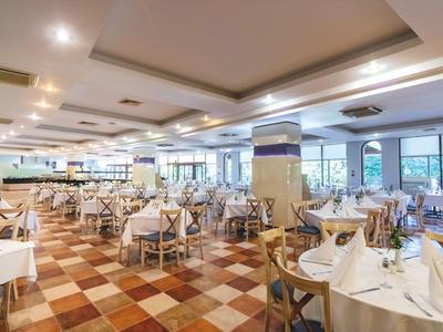 Een groot, licht restaurant met vele gedekte tafels en een geruite vloer.