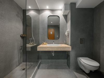 Modernes Hotelbadezimmer mit grauen Wänden, Hänge-WC und begehbarer Dusche.