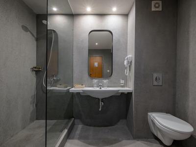 Moderner Hotelbadezimmerbereich mit grauen Wänden, Glasdusche, Waschbecken und Toilette.