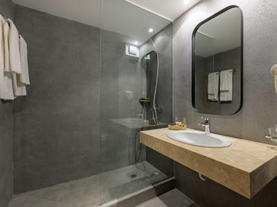Moderner Hotelbadezimmer mit ebenerdiger Dusche, Waschbecken und Handtüchern an der Wand.