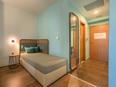 Kleine hotelkamer met eenpersoonsbed, blauwgroene muren en een grote spiegel in de hal.