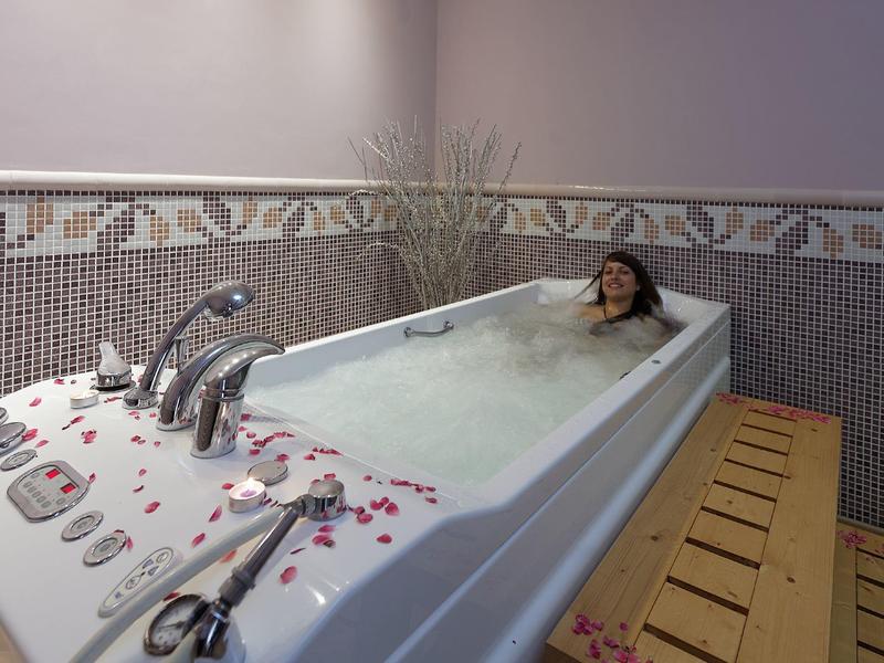 Vrouw ontspant in een bubbelbad met rozenblaadjes in een wellnessruimte.
