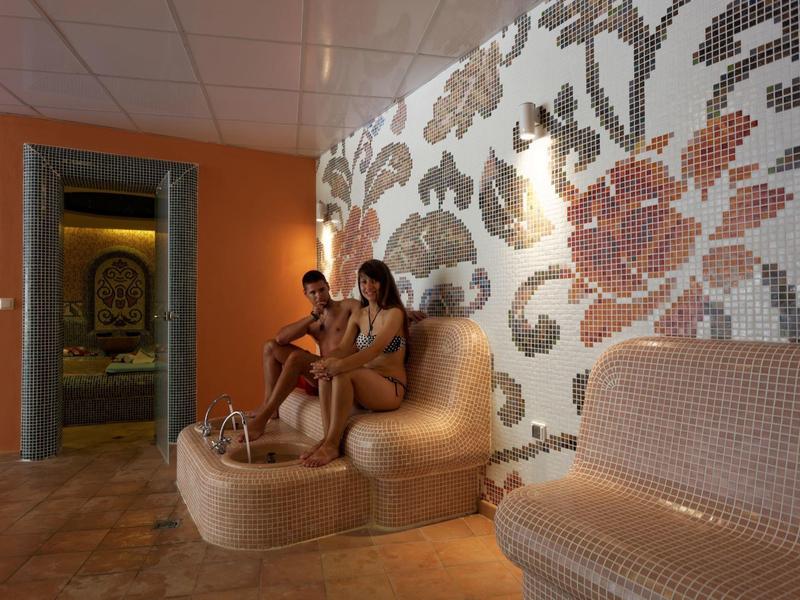 Twee vrouwen ontspannen in een stijlvolle spakamer met mozaïektegels en warm licht.