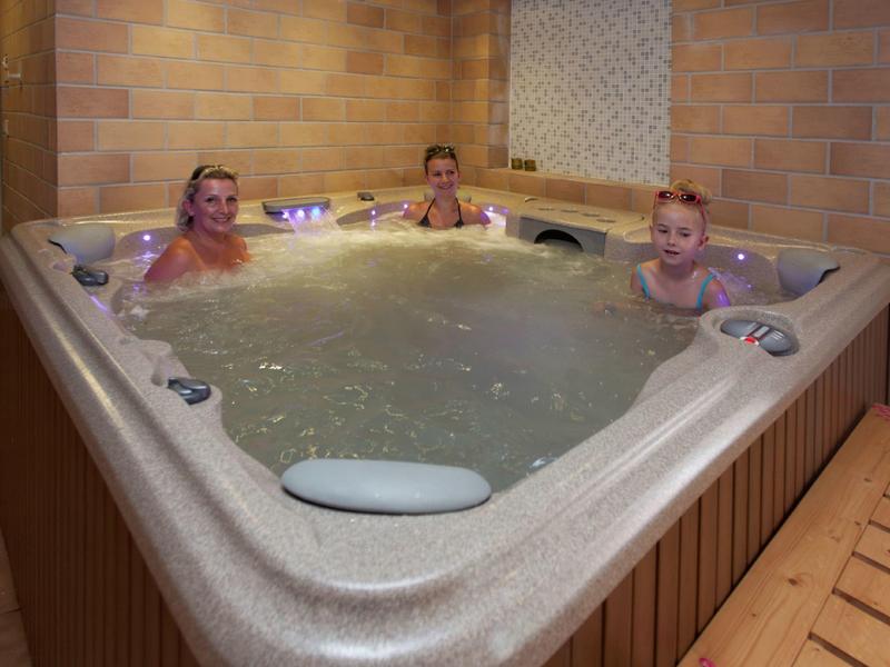 Drie personen ontspannen in een grote bubbelbad in een hotelspa.