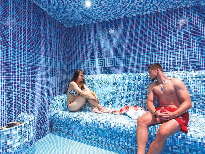 Een man en vrouw ontspannen in een blauwe mozaïekspa met peelingzout.