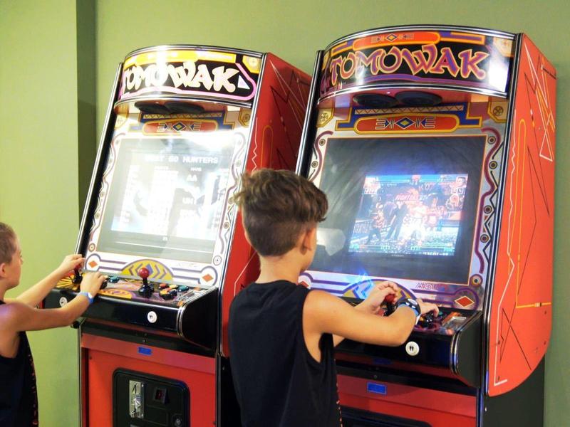 Twee kinderen spelen op arcadeautomaten in een lichte kamer.
