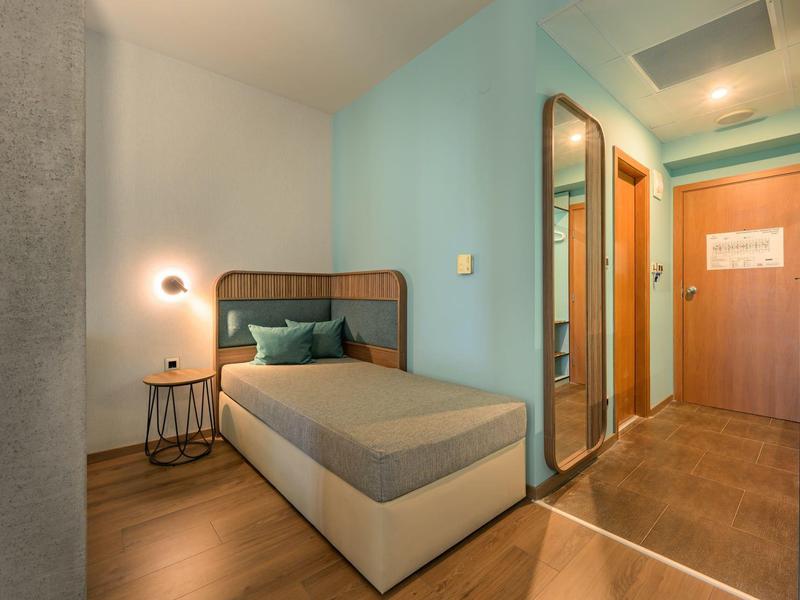 Modern hotelkamer met comfortabel bed, bedlampje en grote spiegel bij de ingang.