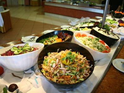 Verschiedene bunte Salate in Schüsseln auf einem Buffet mit Gemüse und Kräutern dekoriert.