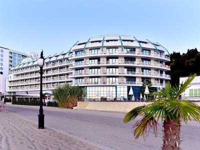 Großes, modernes Hotelgebäude mit Balkonen, davor Palmen und Laternen auf breitem Bürgersteig.