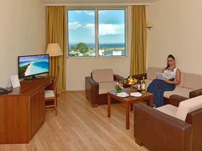 Helles Wohnzimmer mit Holzfußboden, braunen Möbeln, Fensterblick auf Meer und Frau auf Sofa.