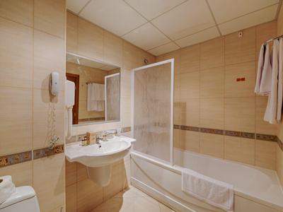 Helles Badezimmer mit Waschbecken, Badewanne, Spiegel und beigefarbenen Wandfliesen.