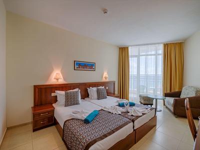 Helles Hotelzimmer mit zwei Einzelbetten, braunen Vorhängen, Sofa und großem Fenster.