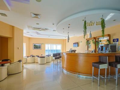 Moderne Hotellobby mit geschwungenem Tresen, Gardena-Stühlen und gemütlichen Sitzgruppen bei Tageslicht.