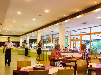 Area del ristorante dell'hotel ben illuminata con ospiti e camerieri, mobili moderni e grandi finestre.