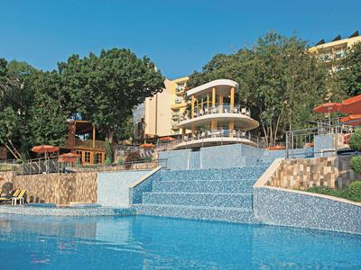 Modern hotel with waterfall and pool, surrounded by trees and sun umbrellas.