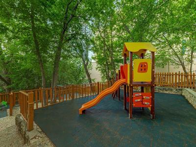 Playground with slide and climbing frame in a wooded area next to a wooden house.
