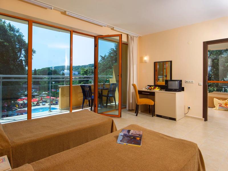 Hotel room with two beds, desk, and balcony overlooking nature.