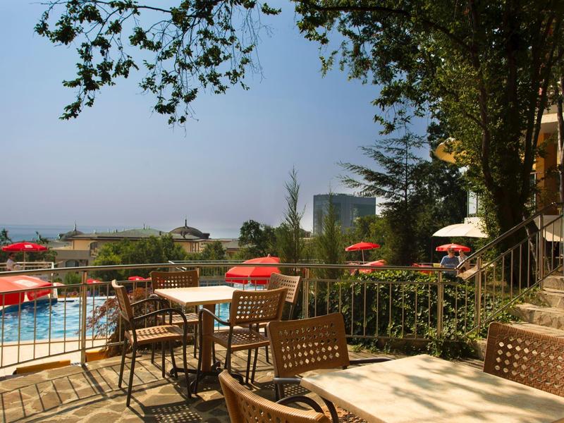 Outdoor area with tables, chairs, and pool surrounded by trees and city view.