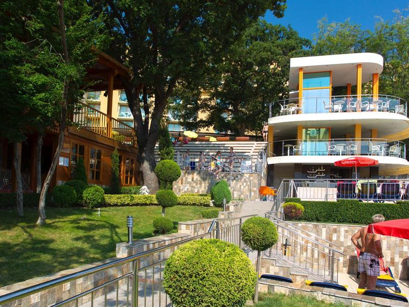 Modern hotel complex with garden, manicured shrubs, and terrace on a sunny day