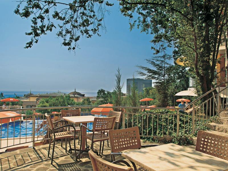 Hotel outdoor area with tables and chairs, pool, and sea view in the background.