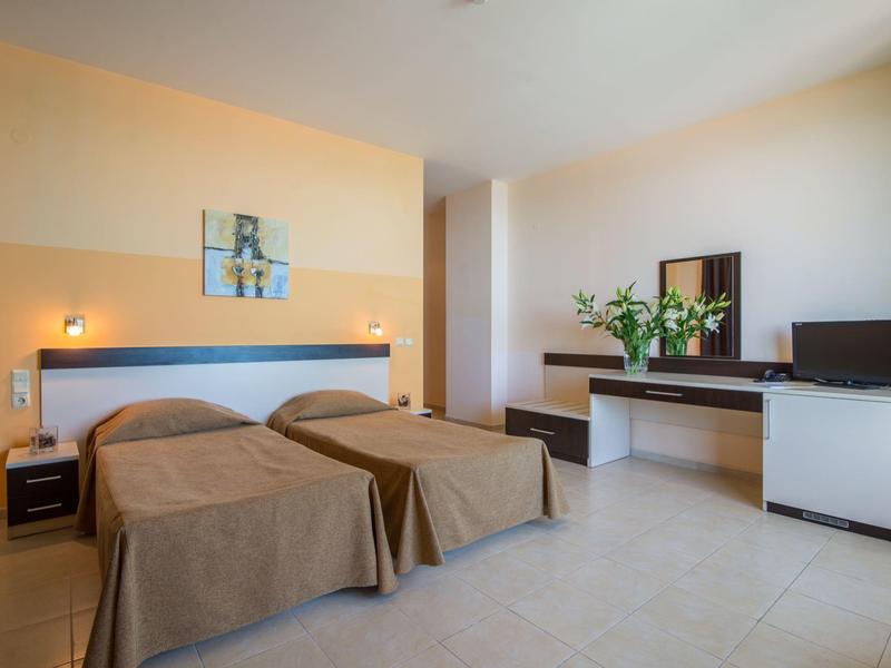 Hotel room with two single beds, desk, TV, and modern decor in warm tones