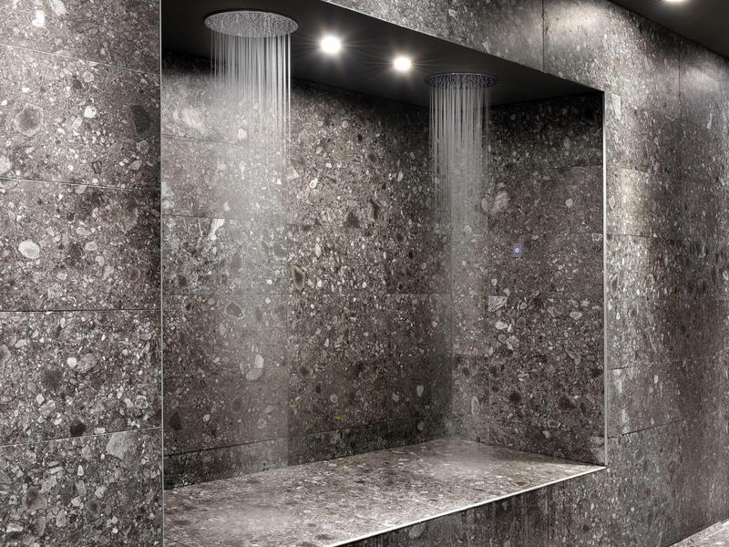 Modern walk-in shower with rain showerheads and gray stone walls.