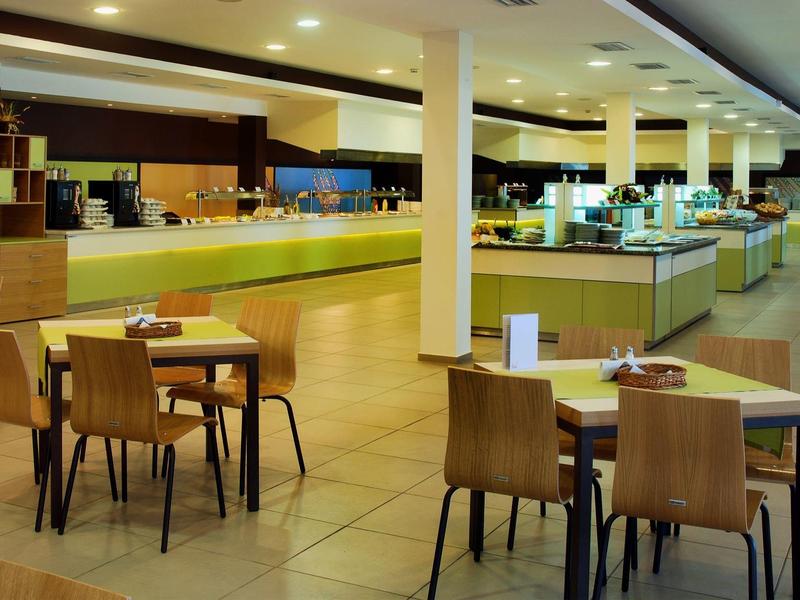 Modern restaurant with wooden tables, chairs, and a long buffet counter.