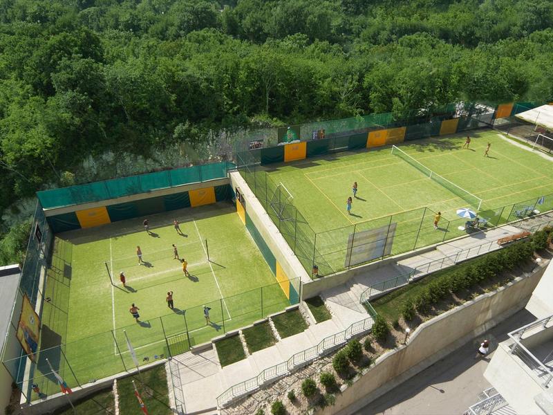 Two small outdoor soccer fields with players, surrounded by trees and buildings.