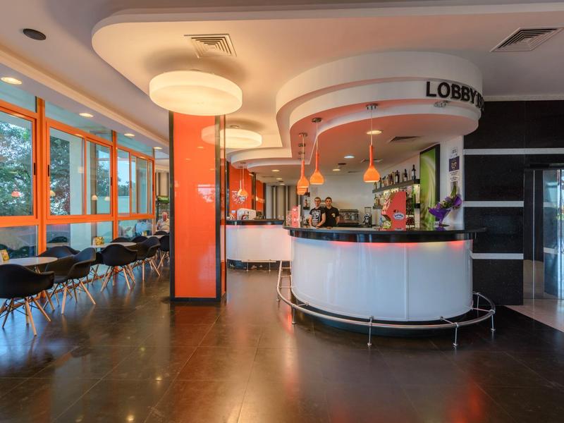 Modern, bright hotel lobby with round reception desk and fabric chairs by windows.
