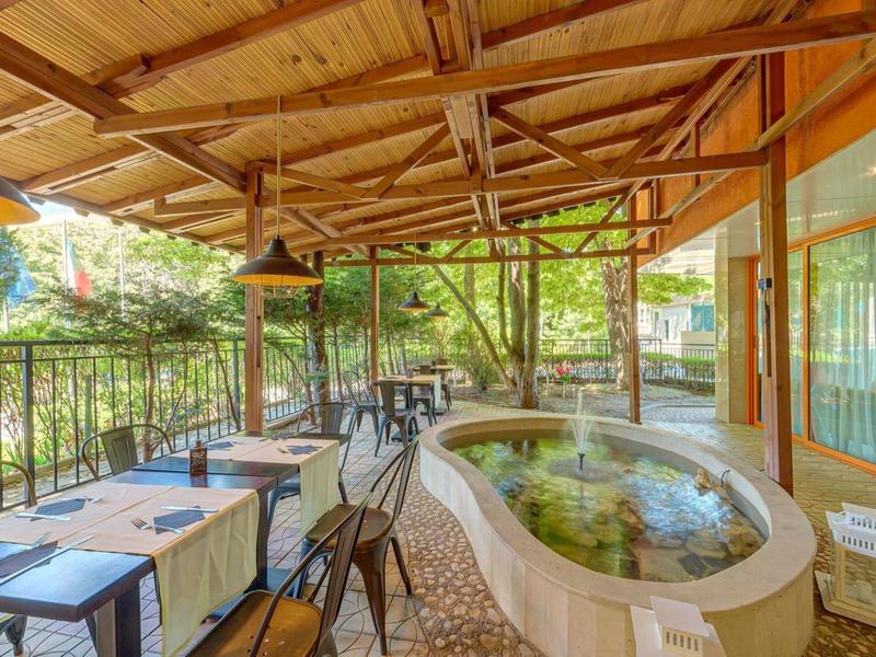 Covered terrace with dining tables and a small pool surrounded by forest.