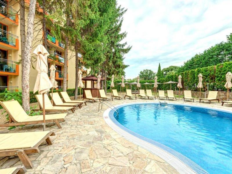 Curved pool with lounge chairs and umbrellas next to a hotel building.