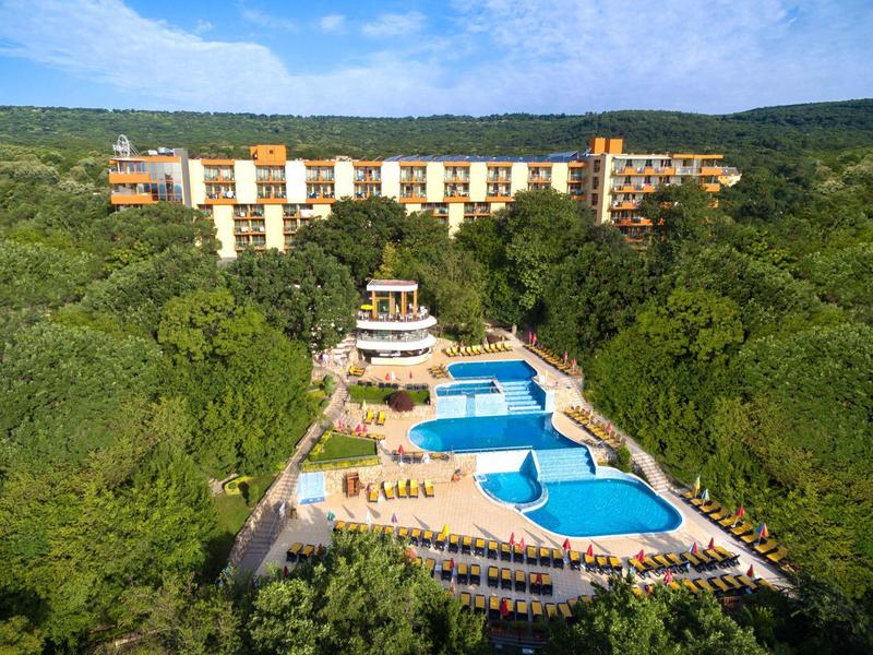 Hotel with large pool areas surrounded by abundant greenery and hills in the background.