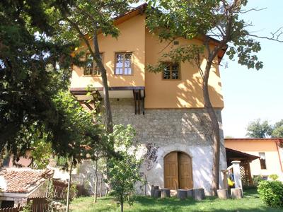 Dwupiętrowy dom wakacyjny z żółtą elewacją i kamienną podstawą, otoczony drzewami i czystym niebem.