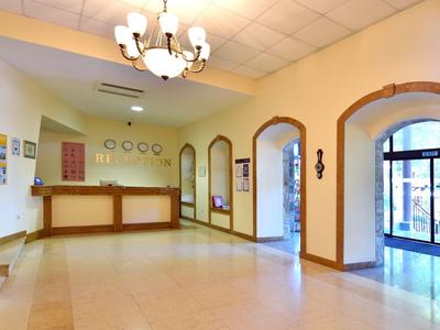 Jasne lobby hotelowe z recepcją, żyrandolem i dużymi oknami łukowymi