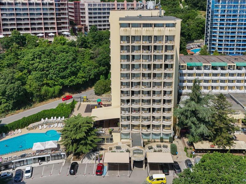 Wielopiętrowy budynek hotelowy z basenem i zielenią w otoczeniu miejskim.