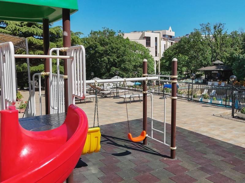 Plac zabaw z czerwoną zjeżdżalnią, huśtawką i zielenią przy czystym niebie