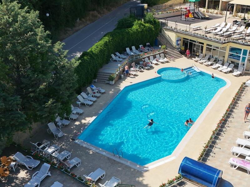 Basen hotelowy z leżakami i gośćmi w otwartej przestrzeni z drzewami.