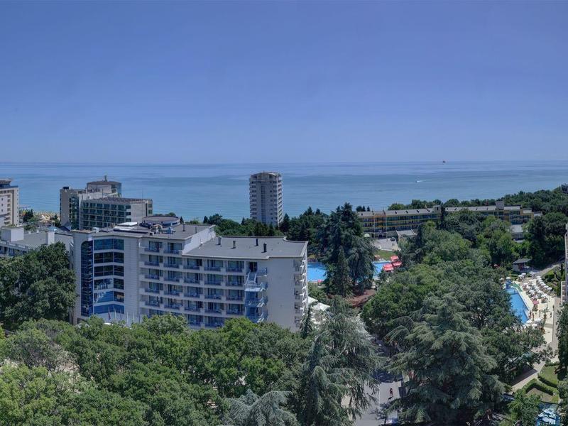 Widok na miasto z wieloma budynkami otoczonymi drzewami i morzem w tle.