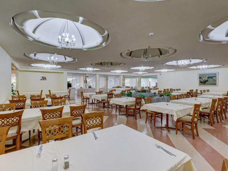 Duża jadalnia z białymi obrusami, drewnianymi krzesłami i okrągłymi lampami sufitowymi.