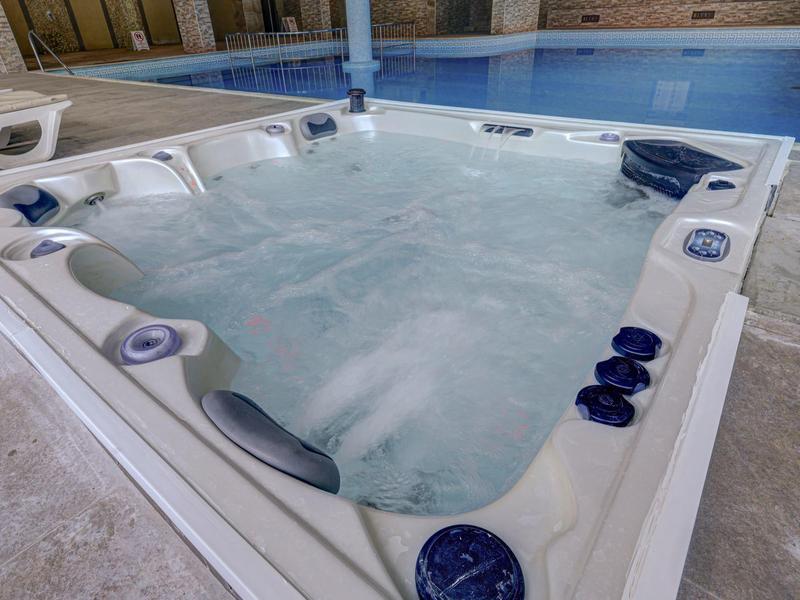 Bulgotująca wanna z hydromasażem obok basenu w pomieszczeniu.