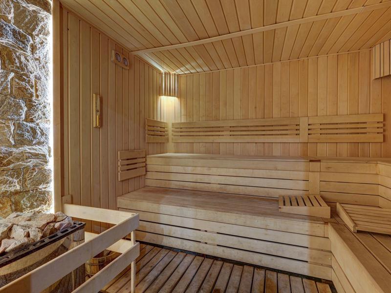 Jasna sauna z drewnianymi ścianami, ławkami i kamiennym piecem z boku.