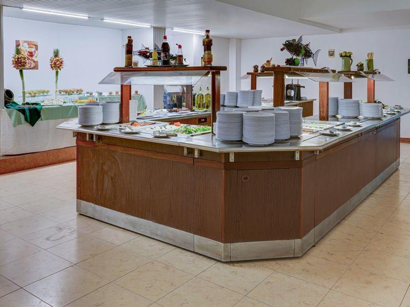 Strefa bufetu z różnymi potrawami i talerzami w jasnym pomieszczeniu.