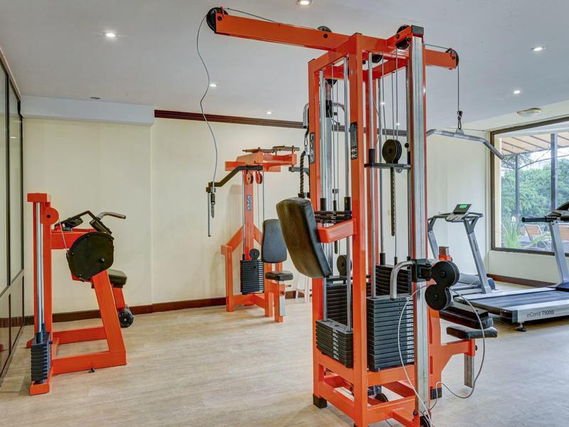 Nowoczesna siłownia z pomarańczowymi urządzeniami fitness i bieżniami przy dużych oknach.