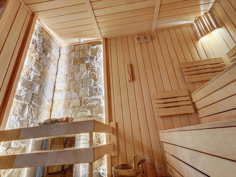 Przytulna drewniana sauna z naturalną kamienną ścianą i ławkami na różnych wysokościach.
