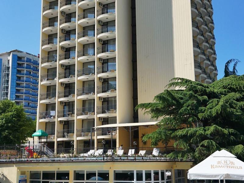 Wysoki budynek hotelowy z pokojami z balkonem obok basenu z pływakami i leżakami.