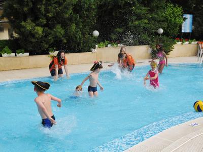 Dzieci bawiące się i skaczące w zewnętrznym basenie hotelowym przy ładnej pogodzie.