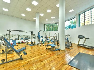 Lichte fitnessruimte met houten vloer, diverse fitnessapparaten en grote ramen.